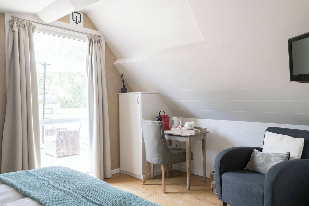 Quarto com cama, escrivaninha, cadeira e televisão.