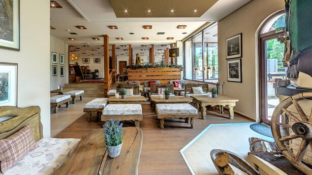 A cozy, rustic-style interior with wooden furniture, a central seating area with a staircase, and a large window providing natural light. - Hotel Moura (Samokov)
