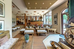 Un interior acogedor de estilo rústico, con muebles de madera, una zona de estar central y una escalera, además de un amplio ventanal que proporciona luz natural.