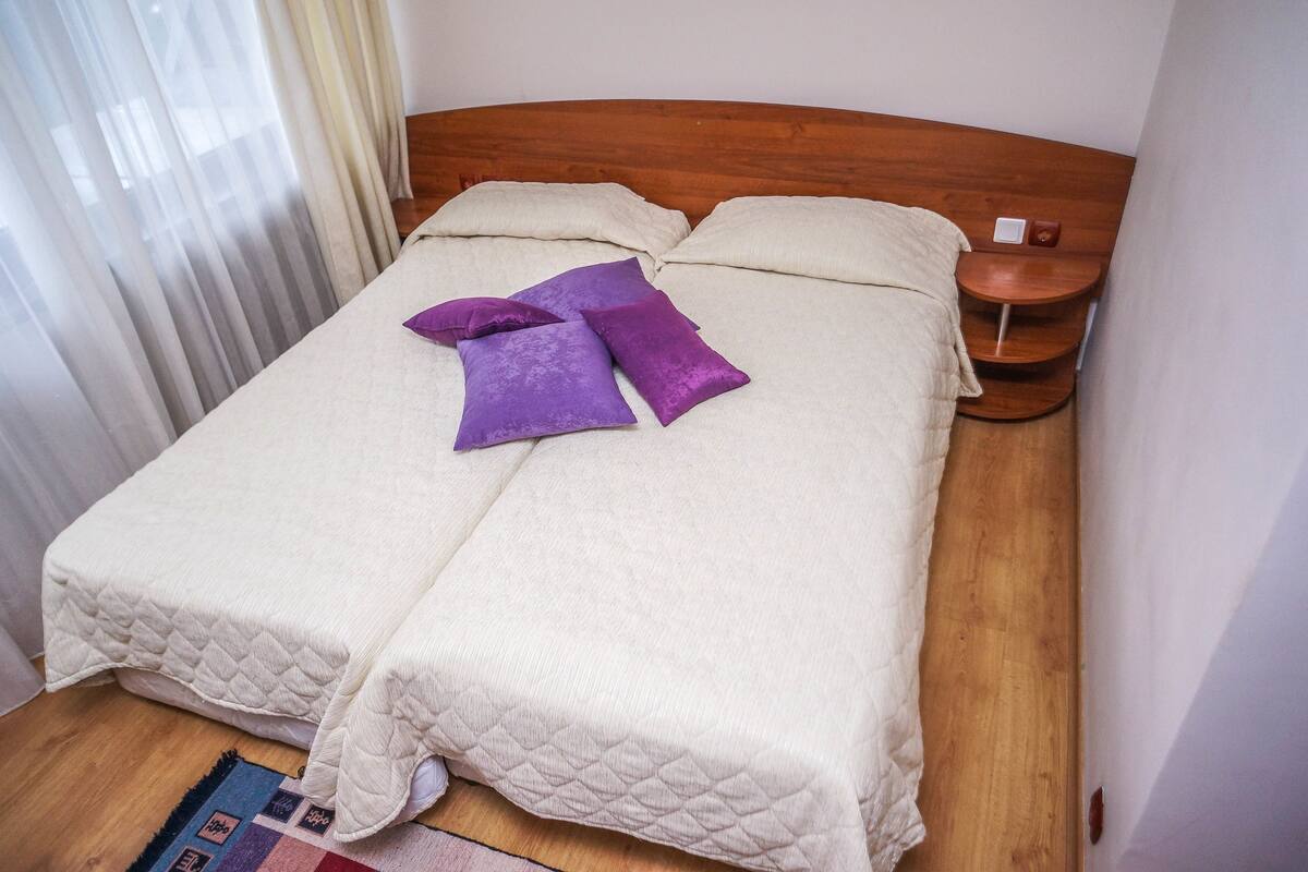 Una cama bien hecha con una cubierta blanca acolchada, dos almohadas y una almohada de acento morada.