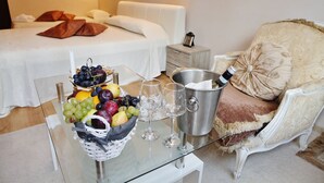 A hotel room with a bed, a nightstand, a glass table with a fruit basket, wine glasses, and a champagne bucket. - Hotel Moura (Samokov)
