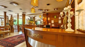 A reception area with a wooden reception desk labeled "RECEPTION," a patterned rug, and a candelabra. - Hotel Moura (Samokov)