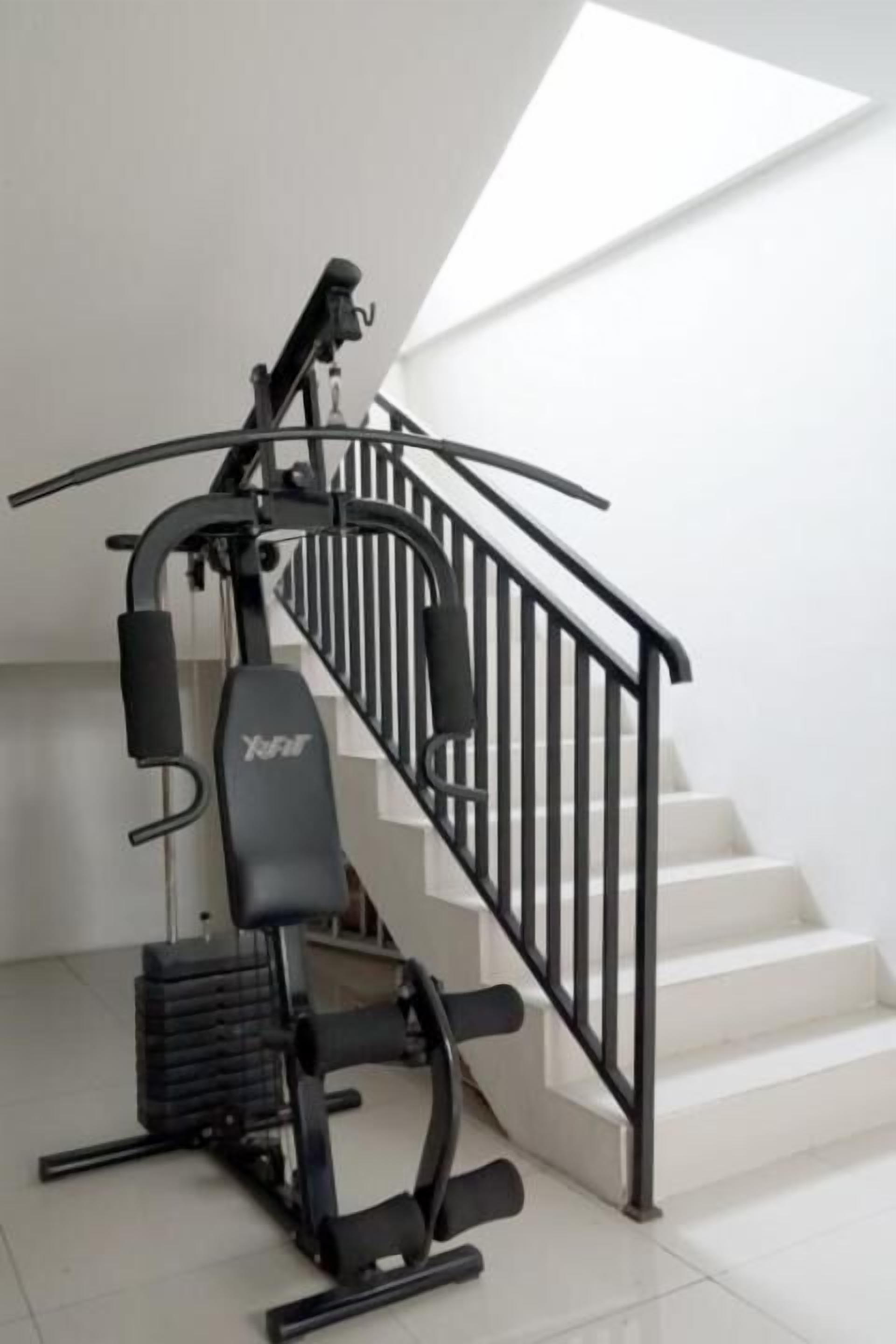 A stairwell with a black exercise machine labeled "YFit" and a white staircase.