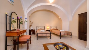 Habitació d'hotel amb dos llits, una taula de fusta amb una cadira, una taula petita amb un bol de fruita i un mirall amb bocs de flors.