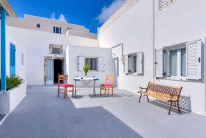 Un patio con un edificio blanco, un banco de madera y una mesa con sillas.