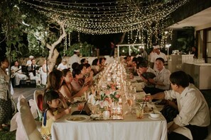 A long dining table set for a formal outdoor event with string lights overhead. - The Longhouse Jimbaran Bali (Jimbaran)