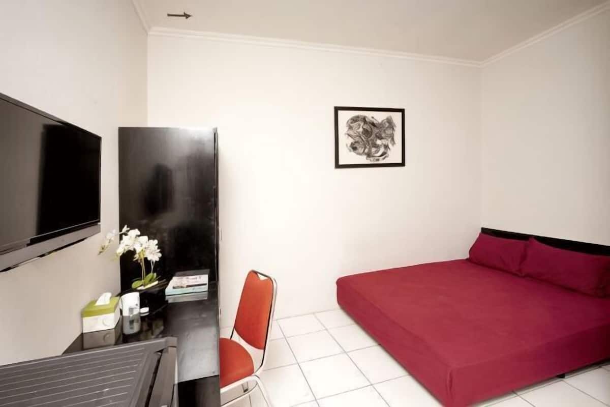 A room with a bed, a TV, a desk with a chair, and a framed picture on the wall.