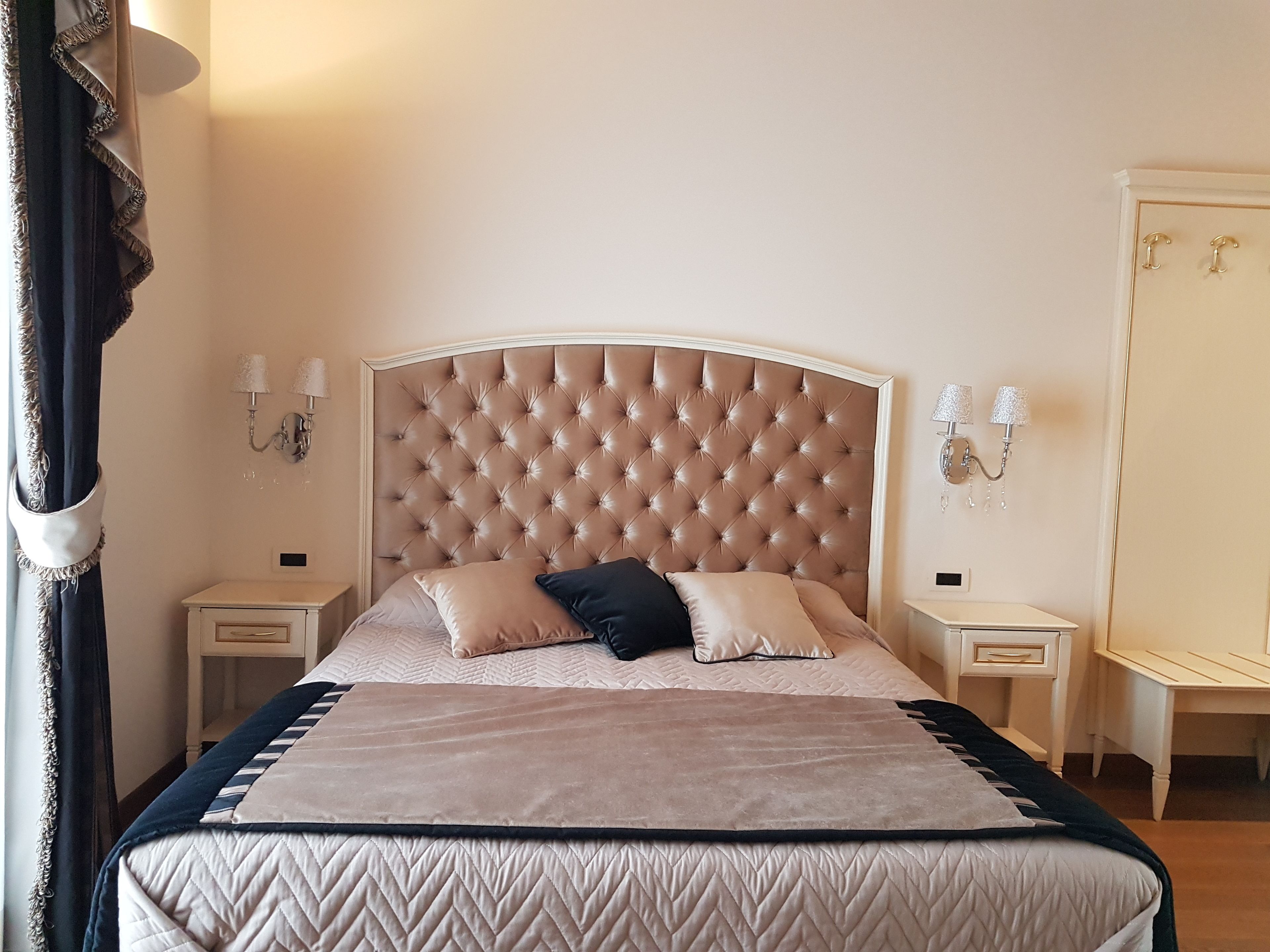A bedroom with a tufted headboard, two bedside tables, a bed with a quilted cover, and a mirror on the wall.