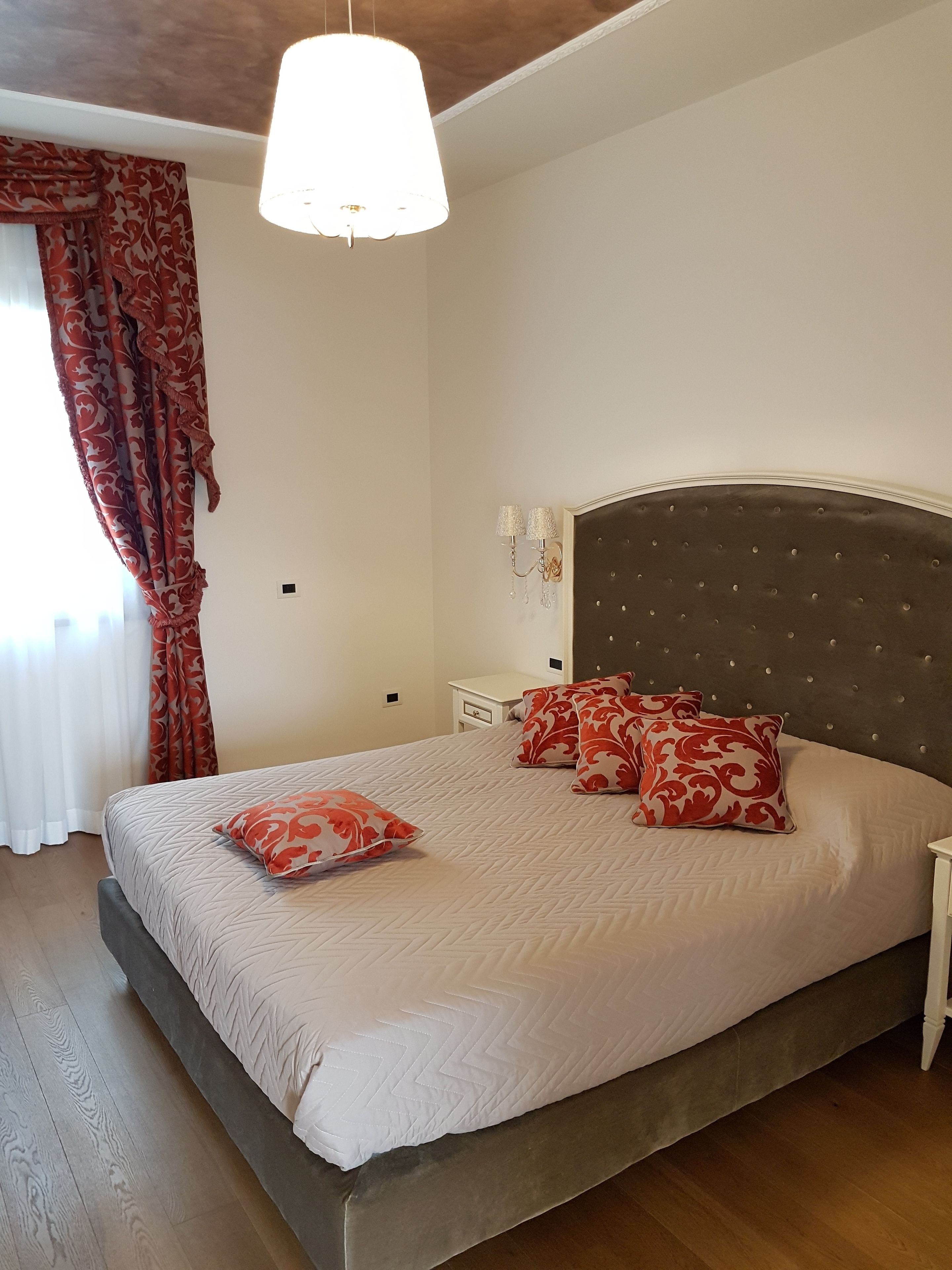 Une chambre à coucher avec un grand lit, une tête de lit capitonnée, une table de chevet et un luminaire suspendu.