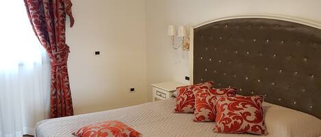 A bedroom with a large bed, a headboard with tufting, a bedside table, and a hanging light fixture.