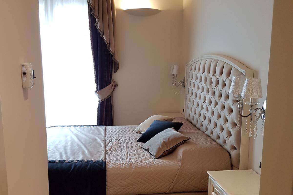 Un dormitorio con cama, mesita de noche, lámpara y ventana con cortinas.