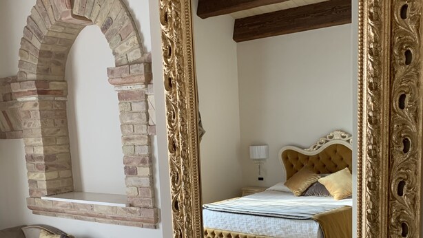 Une pièce avec une arche en briques, un canapé avec des coussins, un lit avec une tête de lit et un grand miroir décoratif.