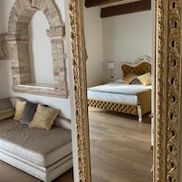 Una habitación con un arco de ladrillo, un sofá con cojines, una cama con cabecera y un espejo grande y ornamentado.
