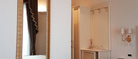A hotel room with a large mirror, a bed, a wardrobe, a bedside table with a lamp, and a small cabinet.
