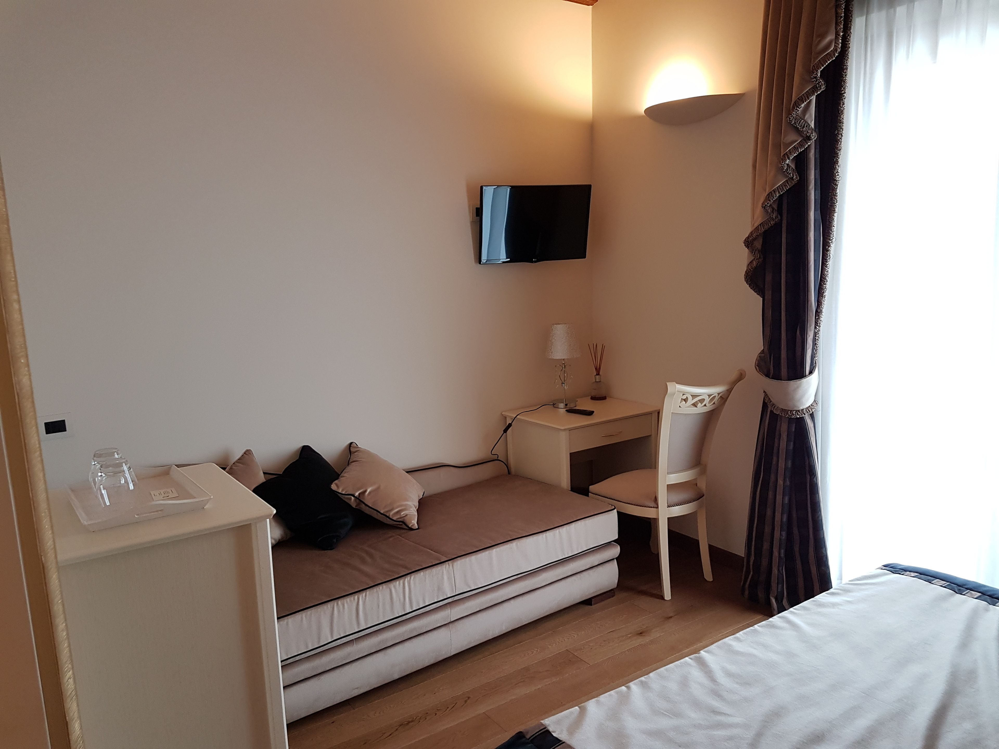 Een knus ingerichte kamer met een bank, een bureau en een stoel. Een flatscreen televisie is aan de muur boven het bureau bevestigd.