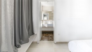 Habitación de hotel con cama, baño con espejo y lavamanos, y pasillo que conduce a otra habitación.