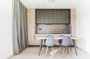 Une cuisine moderne avec des meubles gris, un plan de travail blanc et deux chaises grises aux pieds en cuivre.