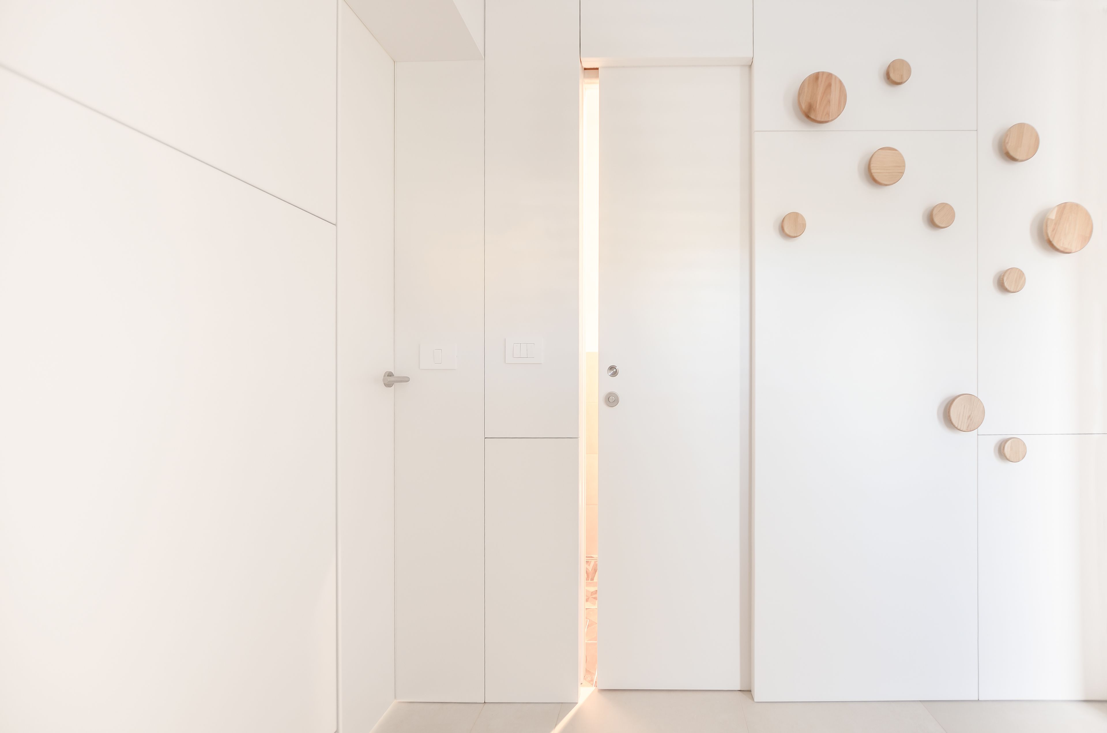 Ein moderner, minimalistischer Raum mit weißen Wänden, einer Holztür und mehreren Holzdrucken an der Wand.