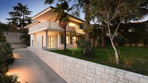 Una casa de dos pisos con un balcón, rodeada de árboles y un césped bien cuidado.