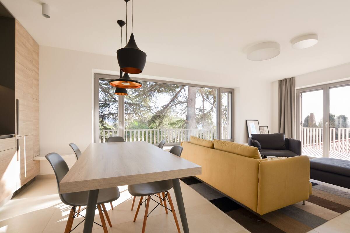 A modern living room with a wooden dining table, black chairs, a yellow sofa, and a black couch.