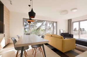 Un salon moderne avec une table à manger en bois, des chaises noires, un canapé jaune et un divan noir.