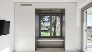 Una habitación moderna con un banco empotrado, un ventanal con vistas a un jardín y un televisor de pantalla plana montado en la pared.