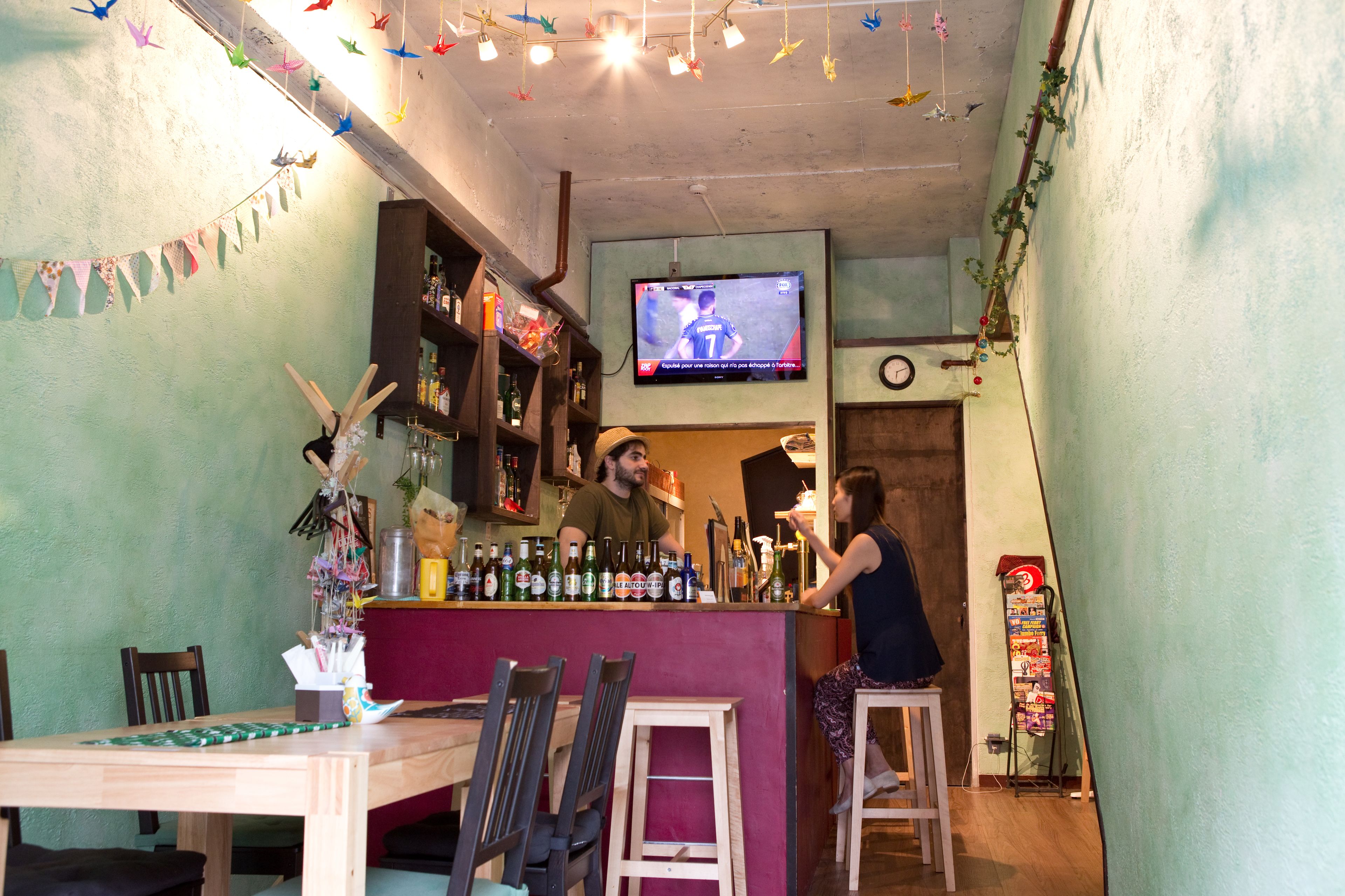 A bar area with a TV screen displaying a sports event, wooden furniture, and a variety of bottles on shelves.