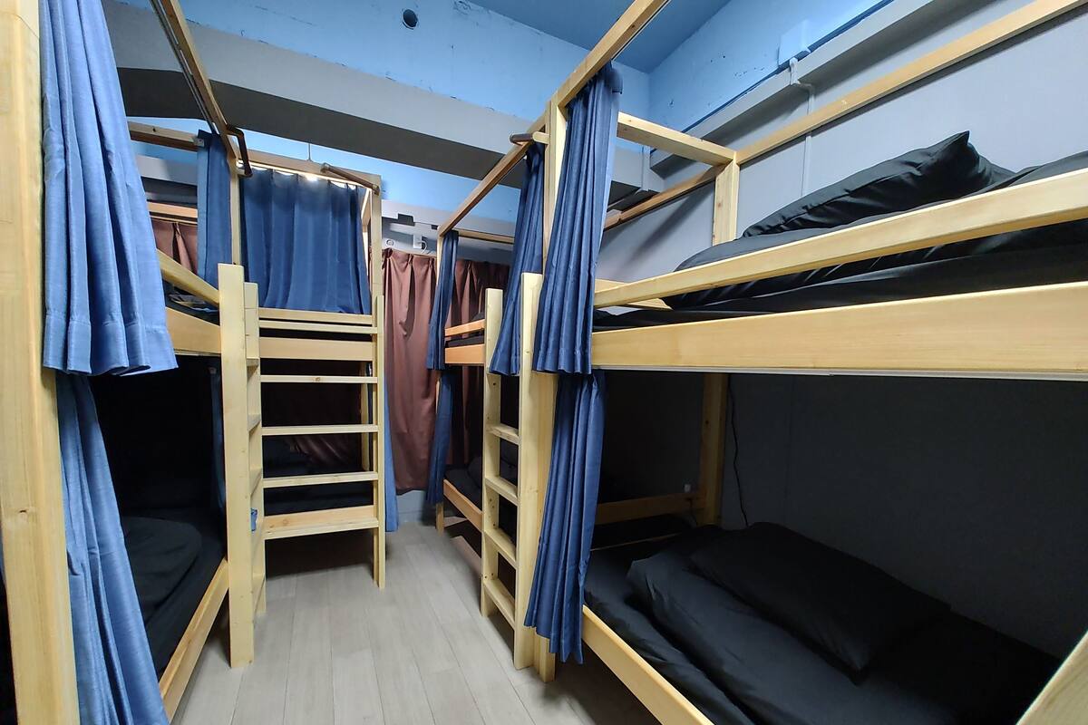 A bunk bed room with wooden frames, blue curtains, and a tiled floor.
