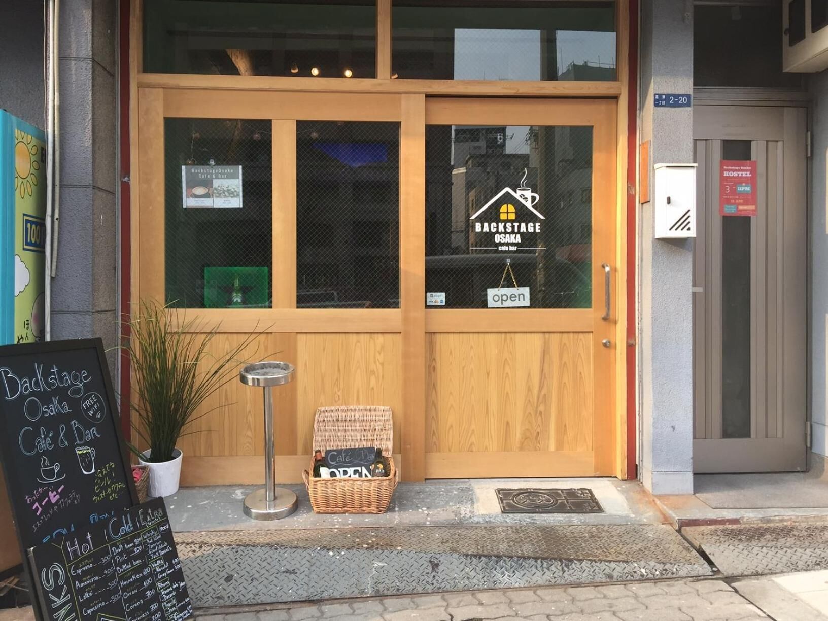Une porte en bois avec une enseigne indiquant « Backstage Osaka Cafe & Bar » et « ouvert ».