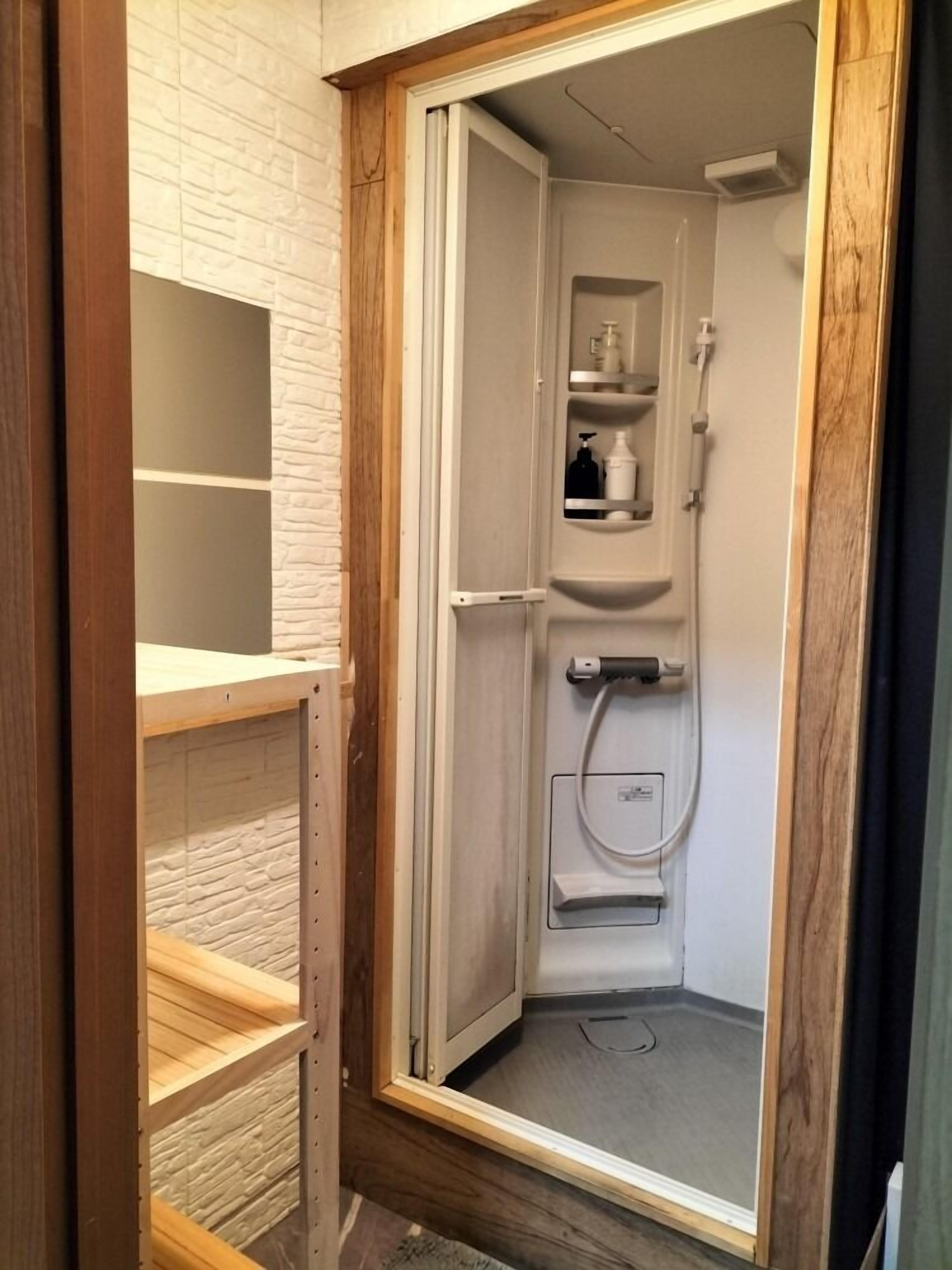 A small, enclosed bathroom with a shower, a toilet, and a shelf with toiletries.
