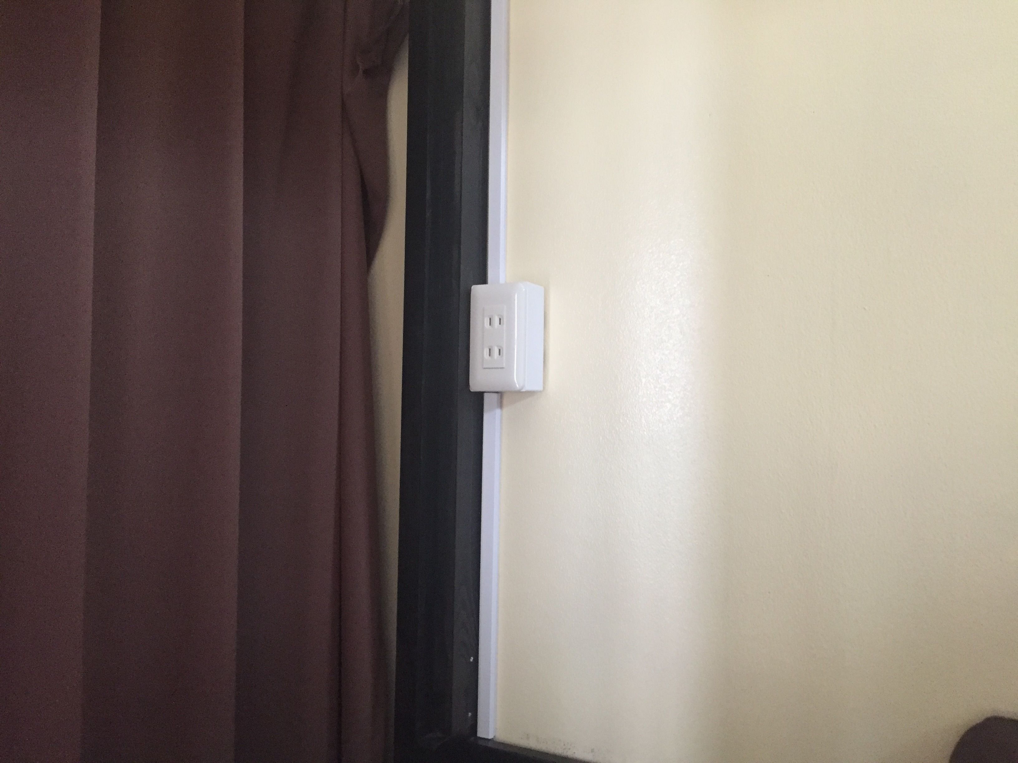 A room with a brown curtain, a white electrical outlet on the wall, and a door frame.