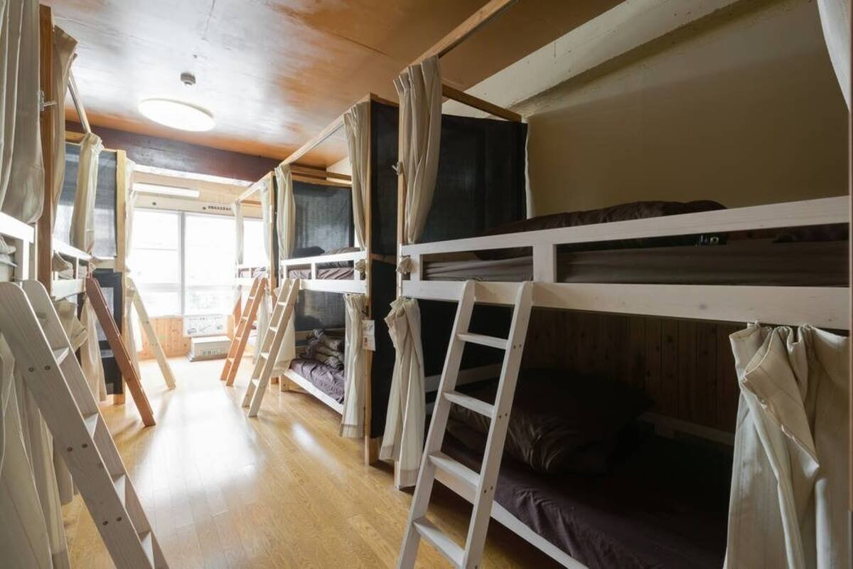 A cabin with bunk beds, wooden floors, and a window with curtains.