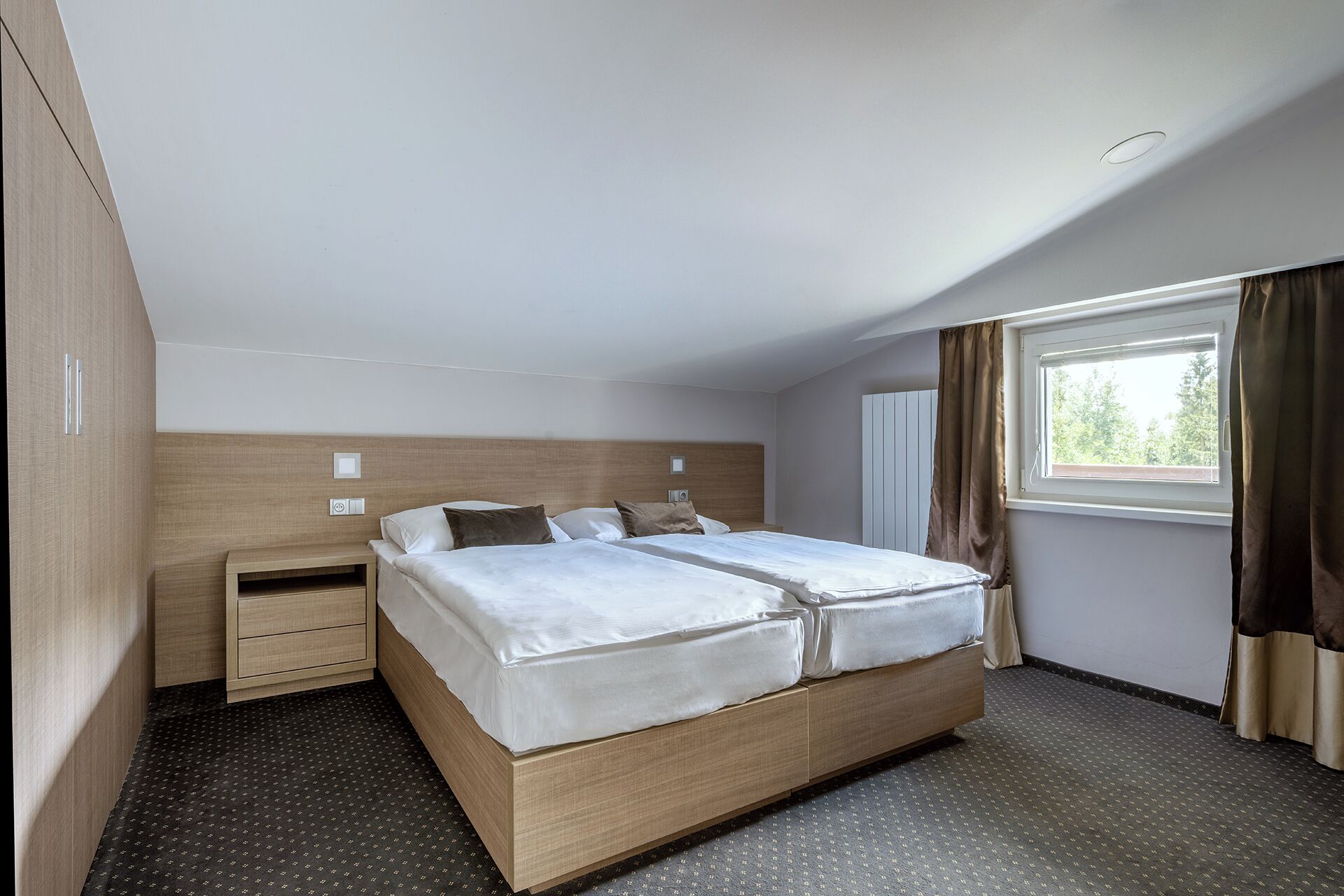 A hotel room with a large bed, a bedside table, a wardrobe, and a window with curtains.