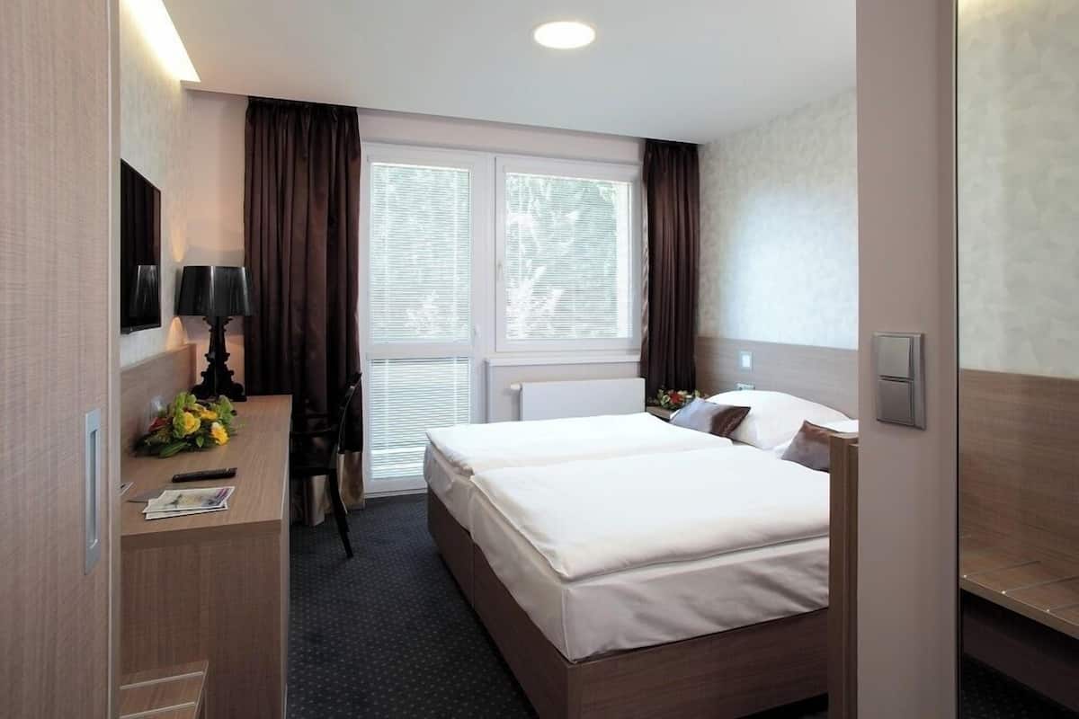 A hotel room with a large bed, a desk with a lamp, a TV, and a window with curtains.