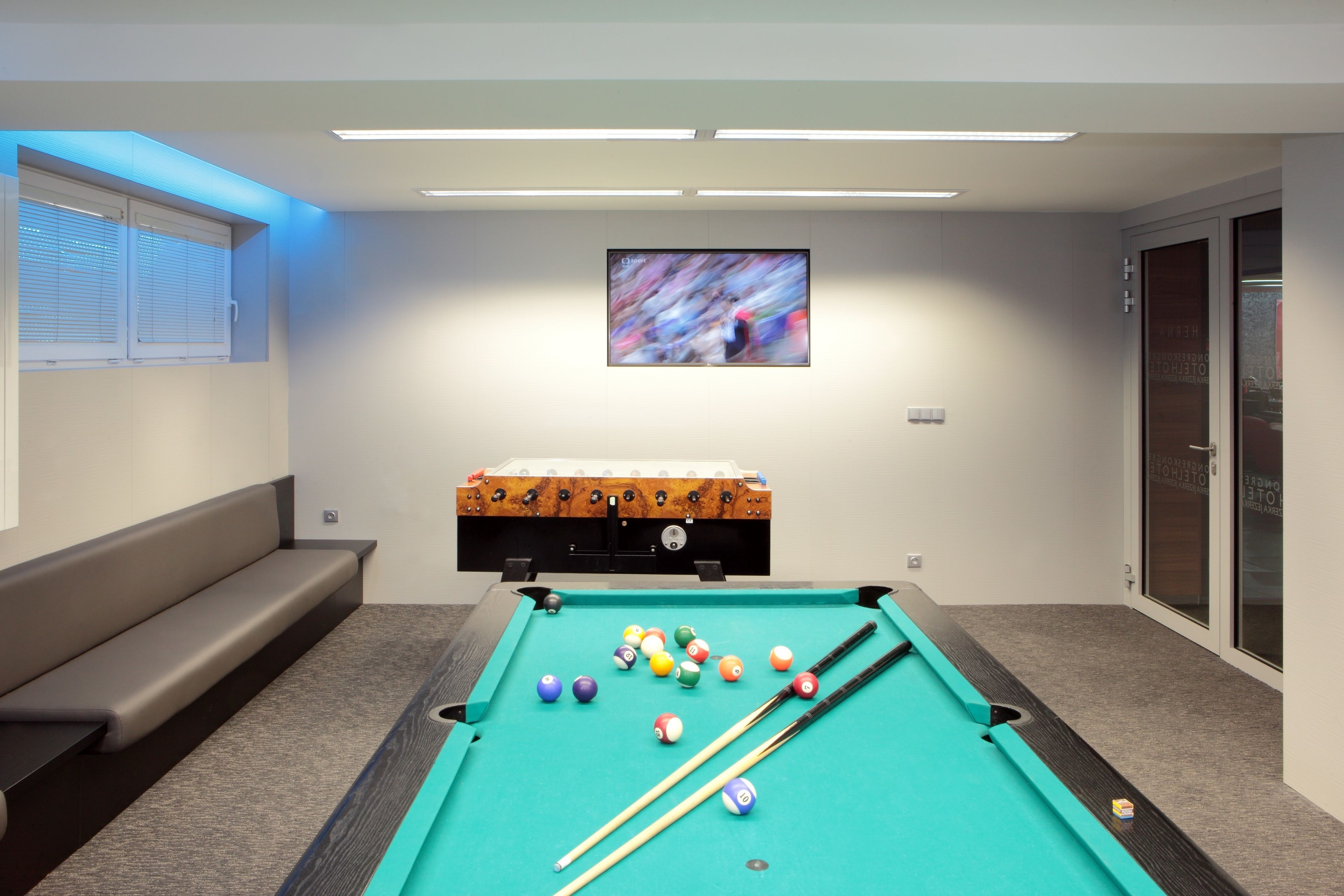 A pool table with balls, a billiard cue, a sofa, and a television screen.