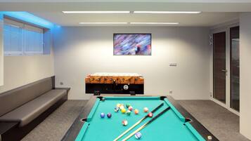 A pool table with balls, a billiard cue, a sofa, and a television screen.