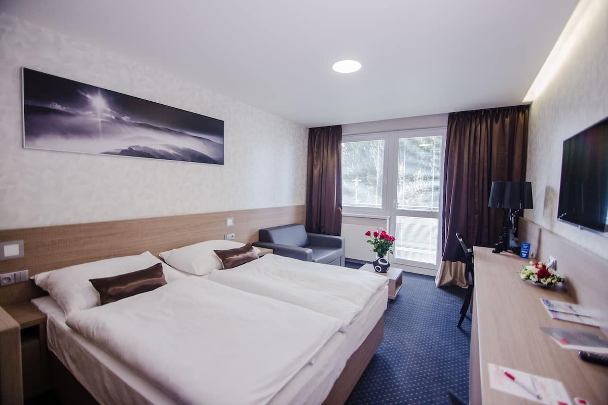 A hotel room with two beds, a desk, a chair, a TV, a window with curtains, and a painting on the wall.