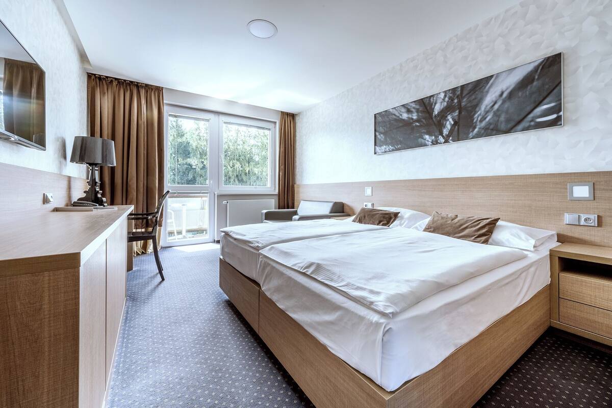 A hotel room with a large bed, a desk, a chair, and a window with curtains.