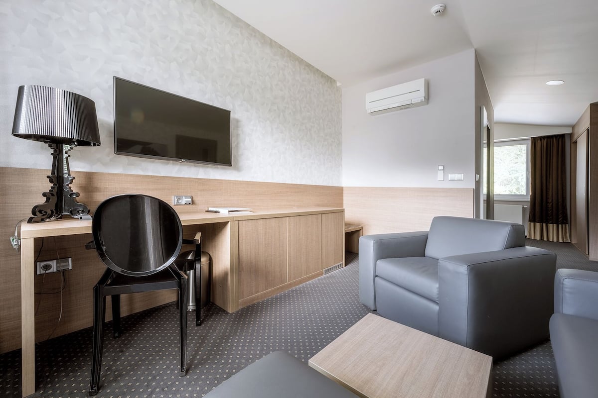 A modern hotel room with a desk, chair, sofa, and a flat-screen TV mounted on the wall.