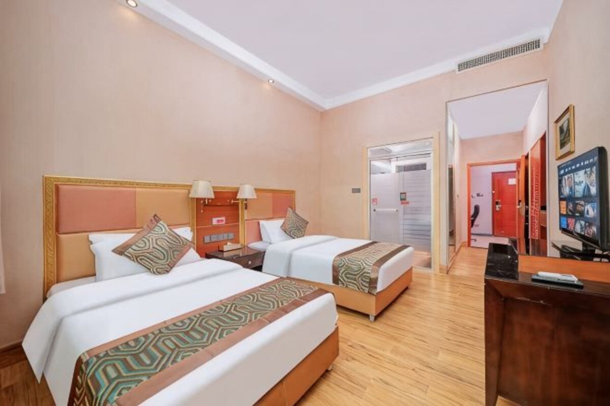 A hotel room with two beds, a desk, a television, and a door leading to another room.