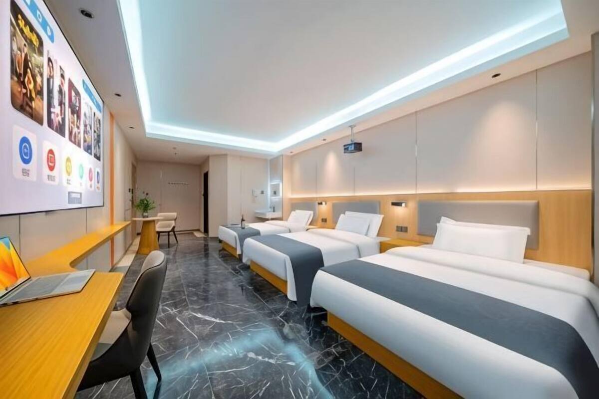 Habitación de hotel con dos camas, un escritorio con una computadora portátil, una mesita pequeña y una pared decorada con cuadros.