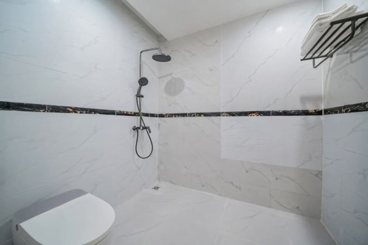 A bathroom with a toilet, a shower with a handheld showerhead, and a towel rack.