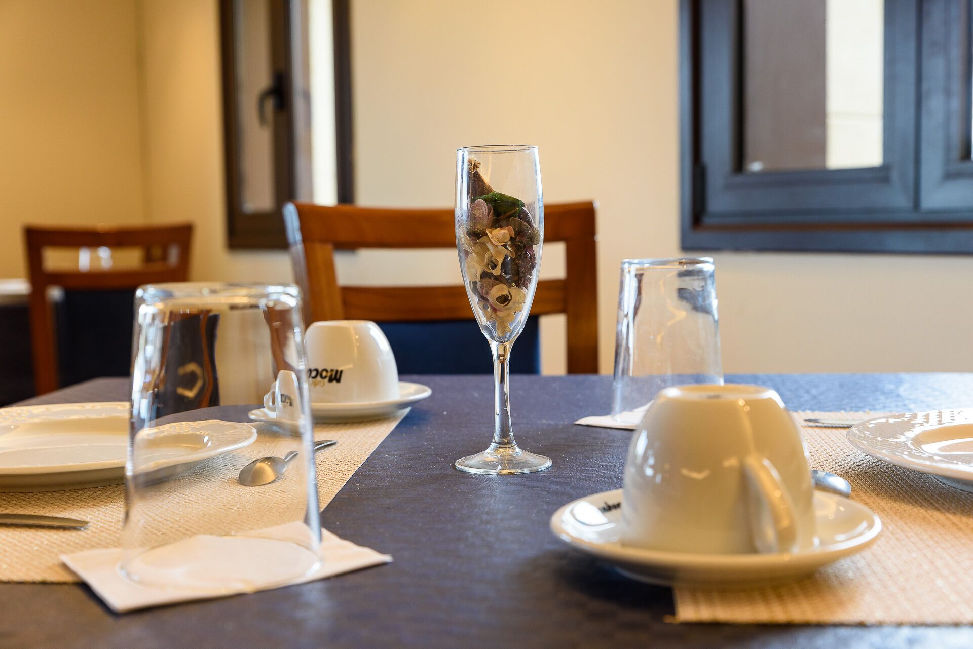 Una mesa de comedor servida con platos blancos, tazas y un vaso de fruta seca.