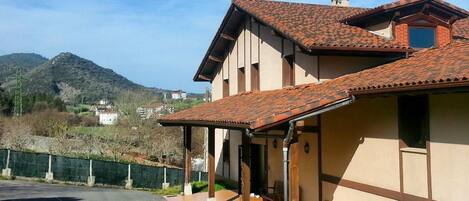 A two-story building with a tiled roof, a covered porch, and a view of a mountainous landscape.