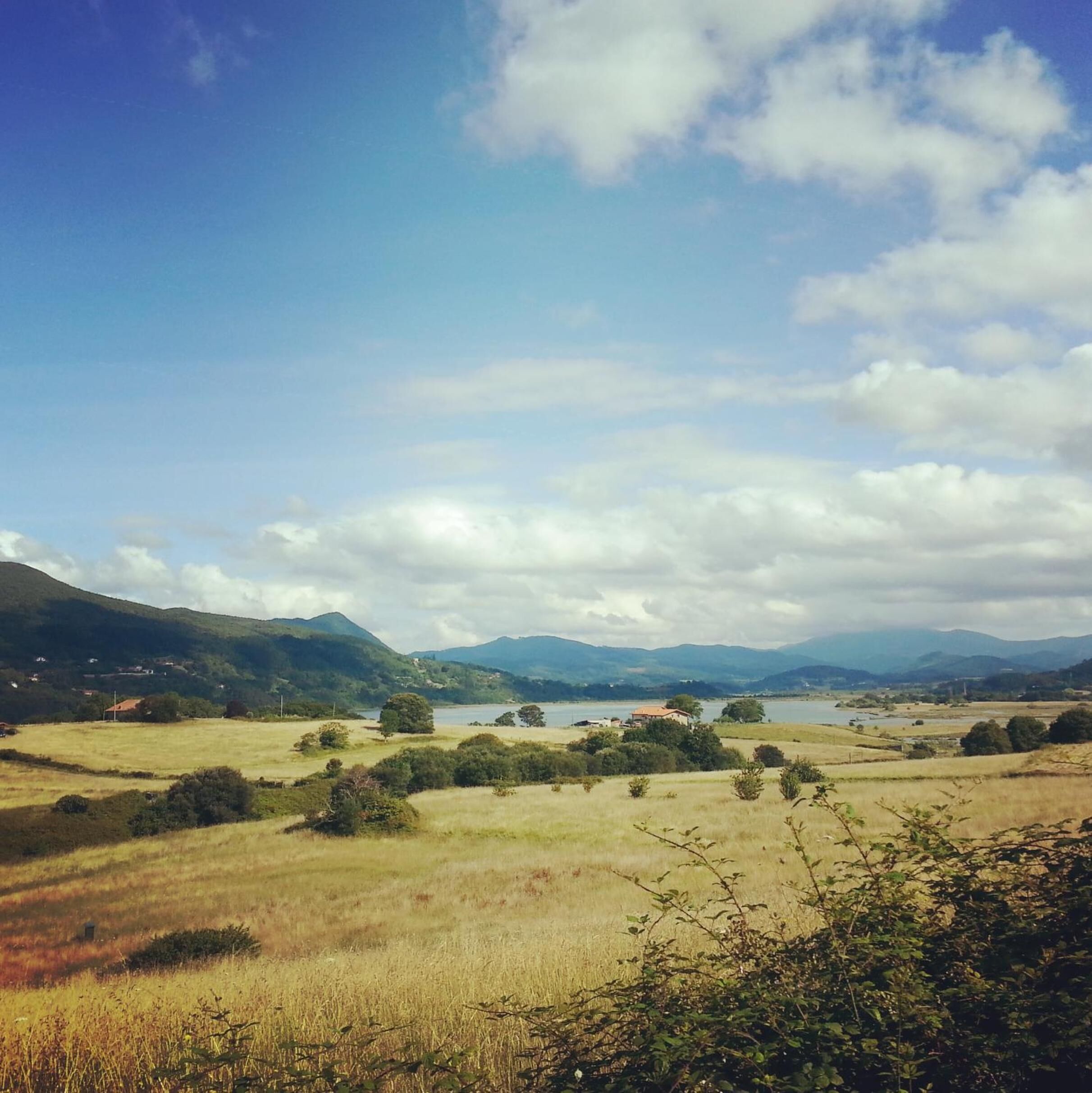 A panoramic view of a rural landscape with rolling hills, a lake, and scattered houses.