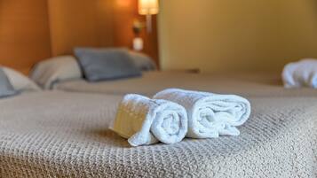A neatly made bed with a textured blanket and two rolled white towels placed on top.