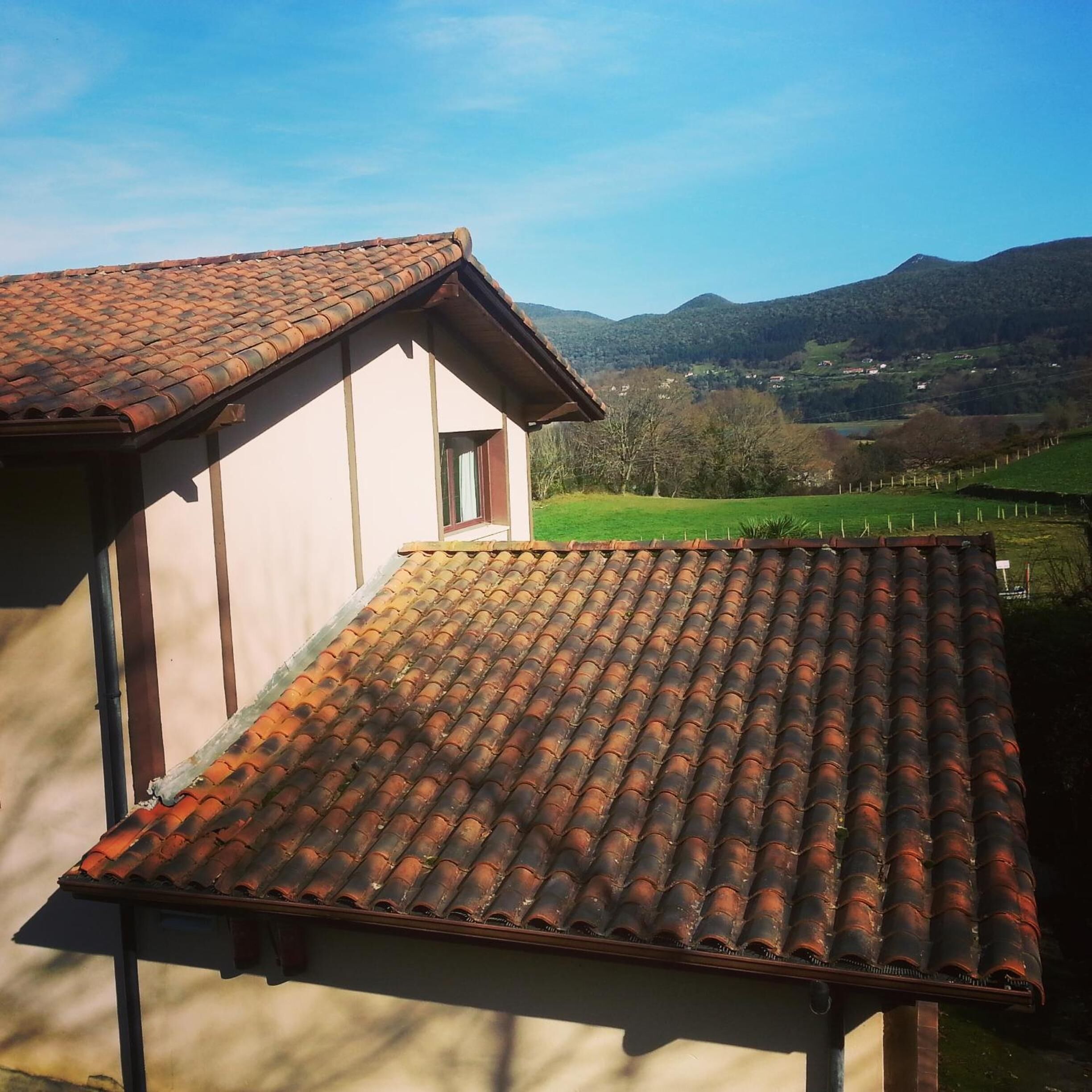 A building with a tiled roof and a view of a green valley and mountains in the background.
