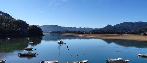 Un lac paisible où sont amarrés des bateaux, entouré de collines boisées et surplombé d’un ciel dégagé.