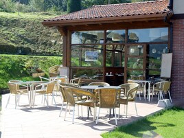 Un patio al aire libre con sillas y mesas de mimbre, un edificio de ladrillo con ventanas amplias y vistas a una colina.