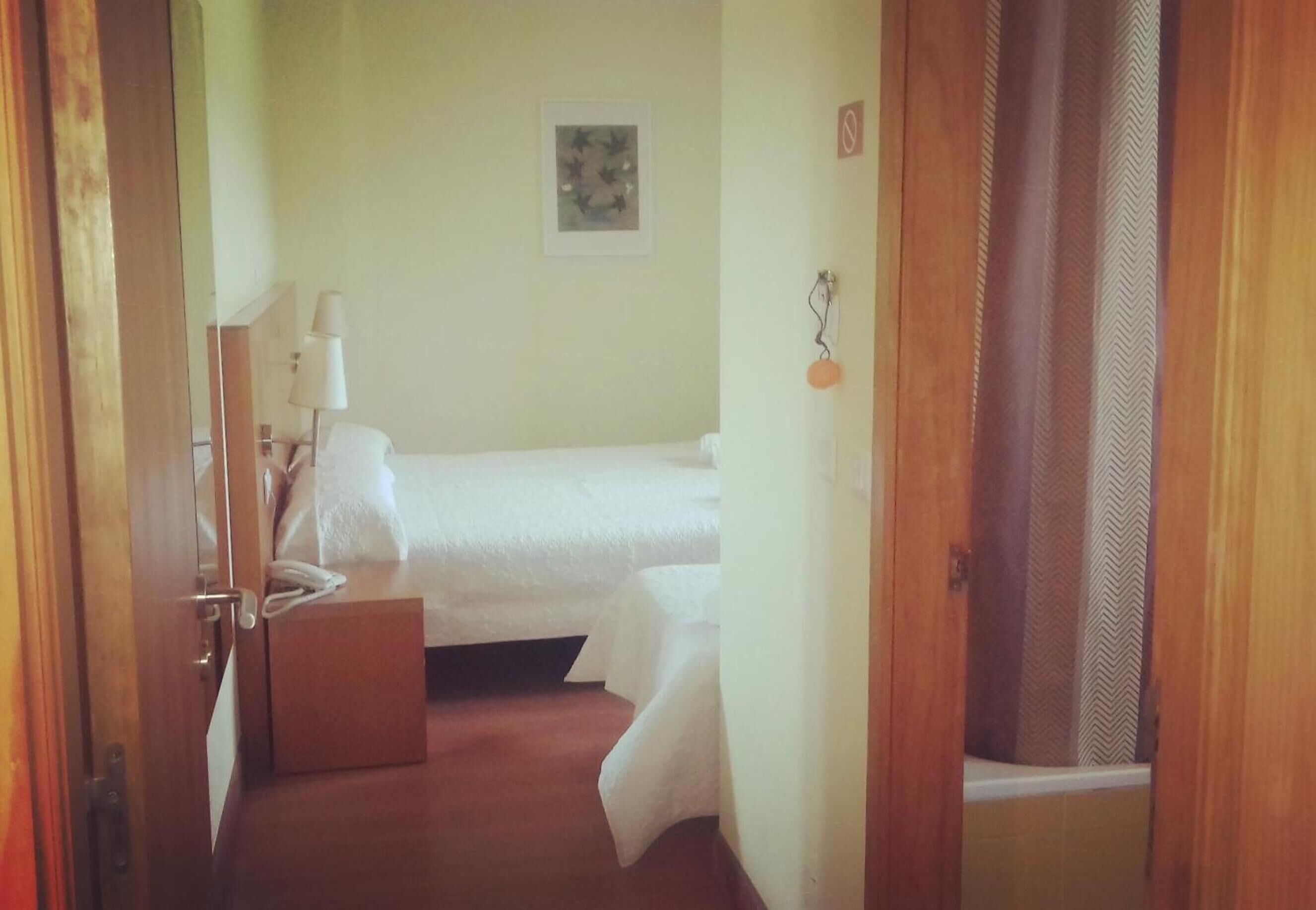 Een hotelkamer met een bed, nachtkastje, lamp en een ingelijste foto aan de muur.